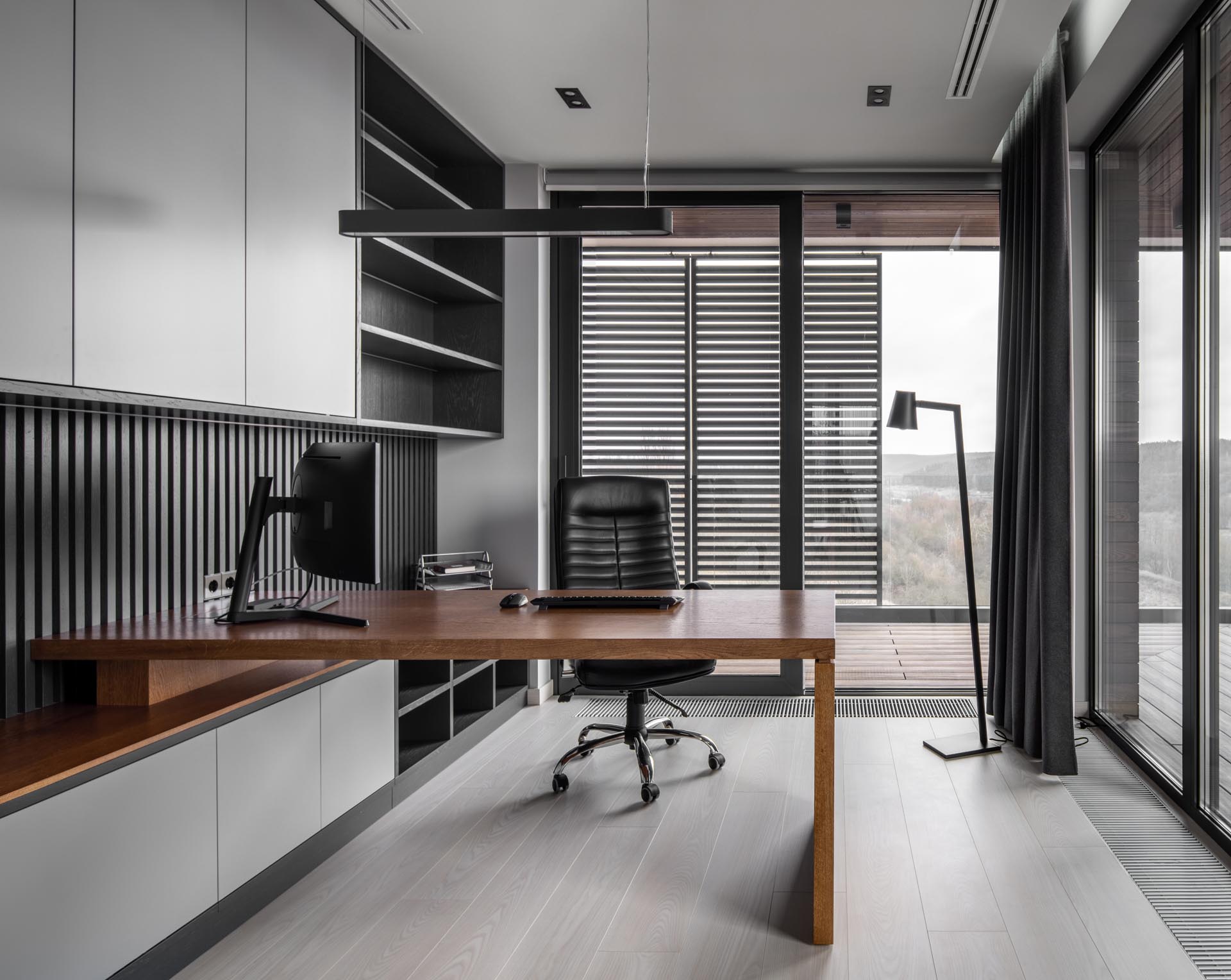 В домашнем офисе есть окна от пола до потолка и встроенная мебель с деревянным столом.