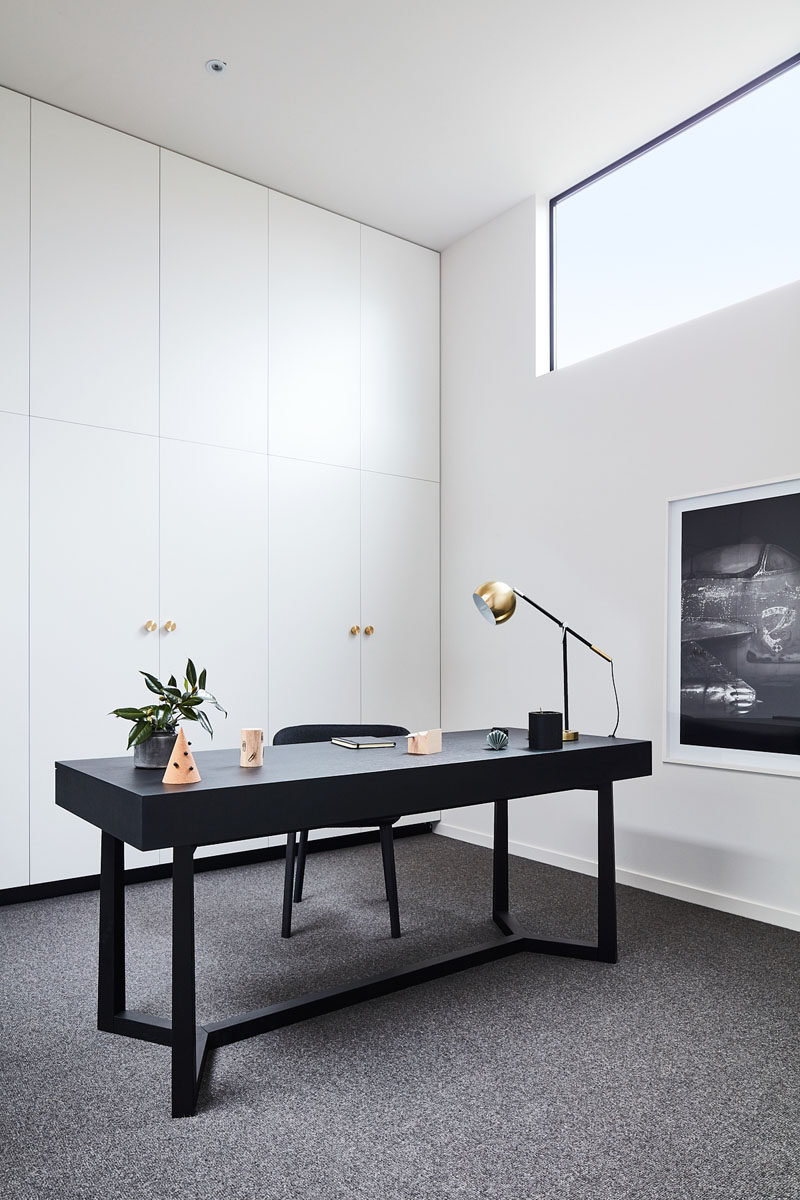  Белые минималистичные шкафы украшают стену в этом домашнем офисе, а черный стол дополняет черные оконные рамы и произведения искусства. #ModernHomeOffice #InteriorDesign 