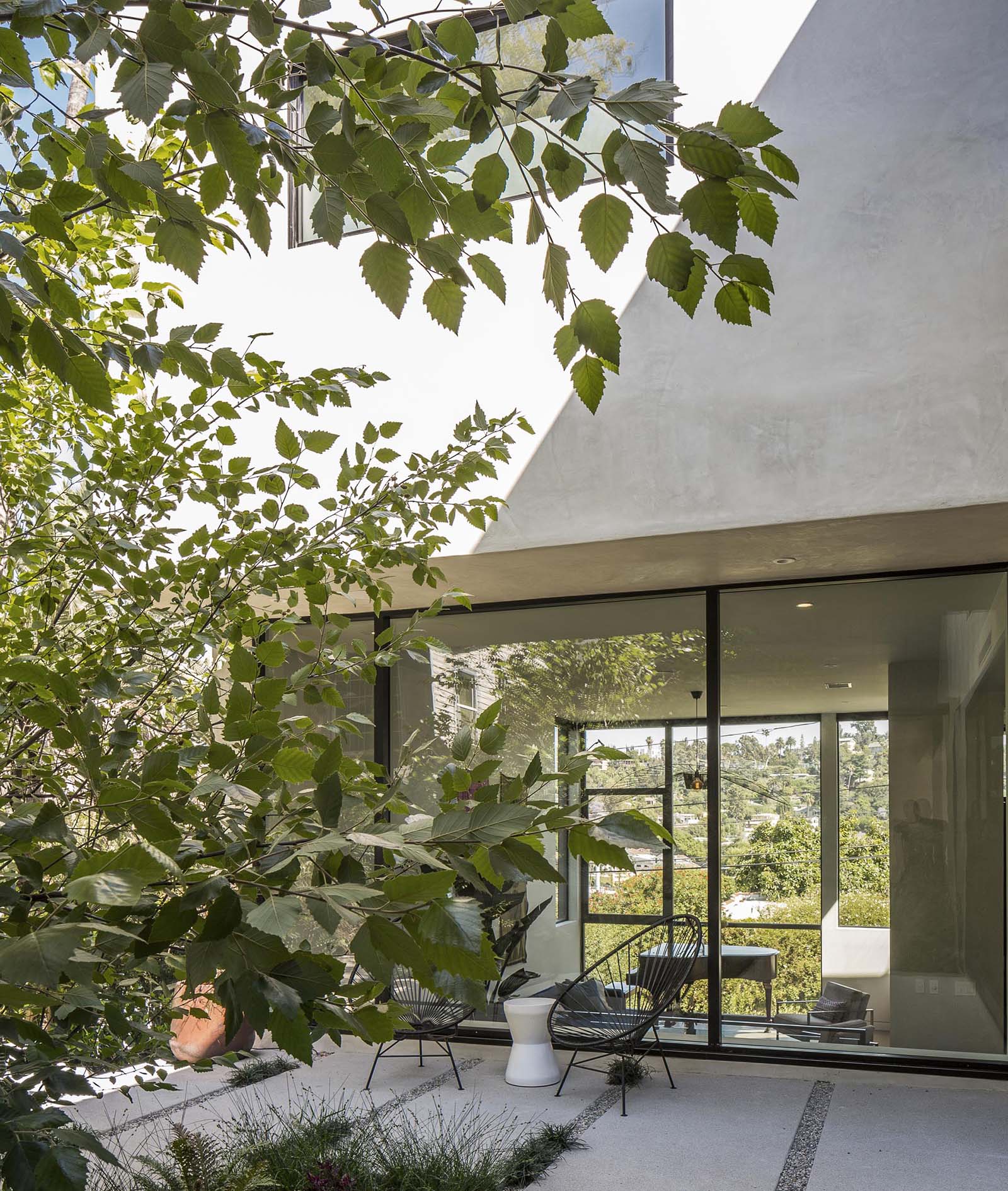 Современный двор с бетонной брусчаткой, галькой, травой и большим деревом.