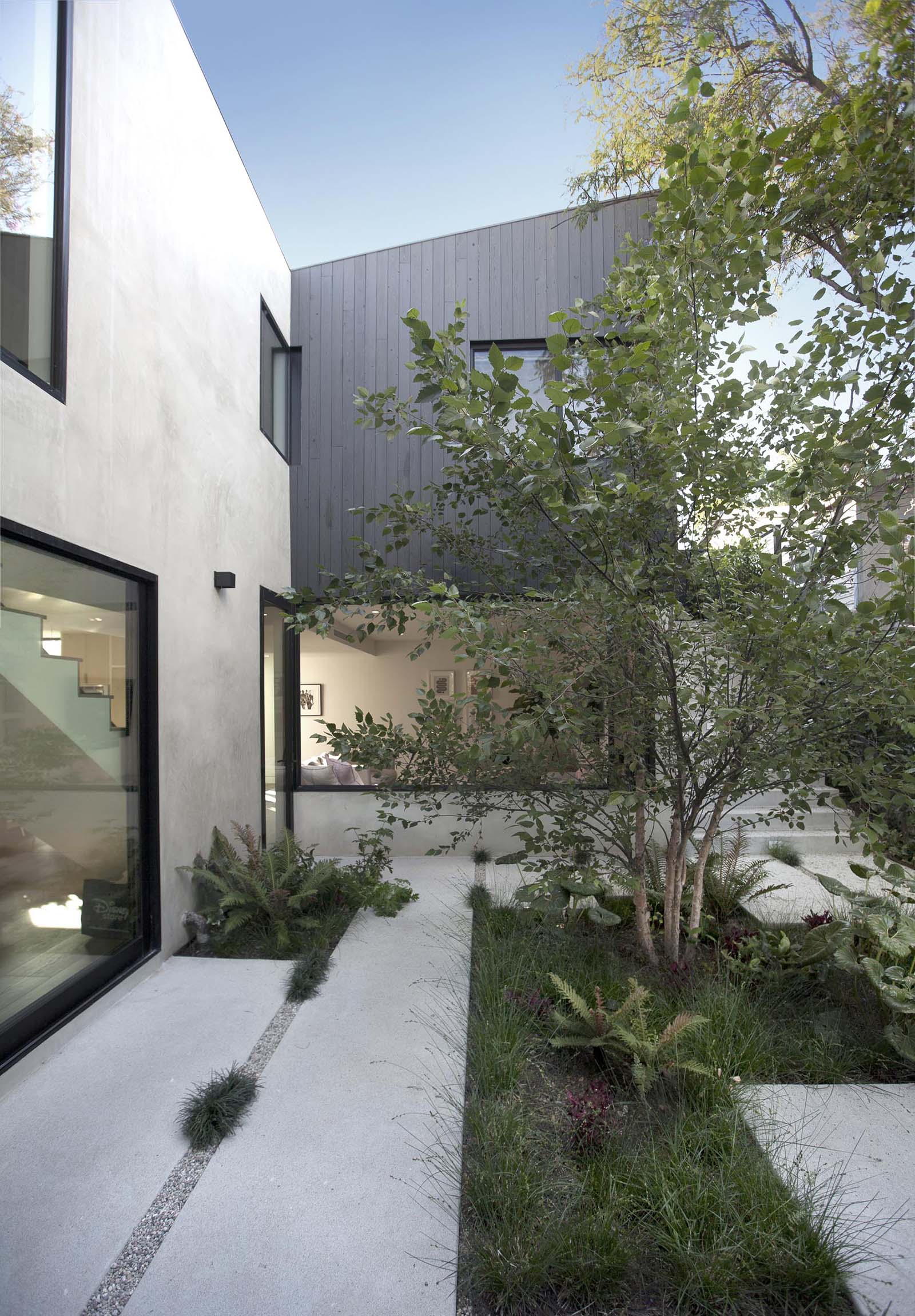 Современный двор с бетонной брусчаткой, галькой, травой и большим деревом.