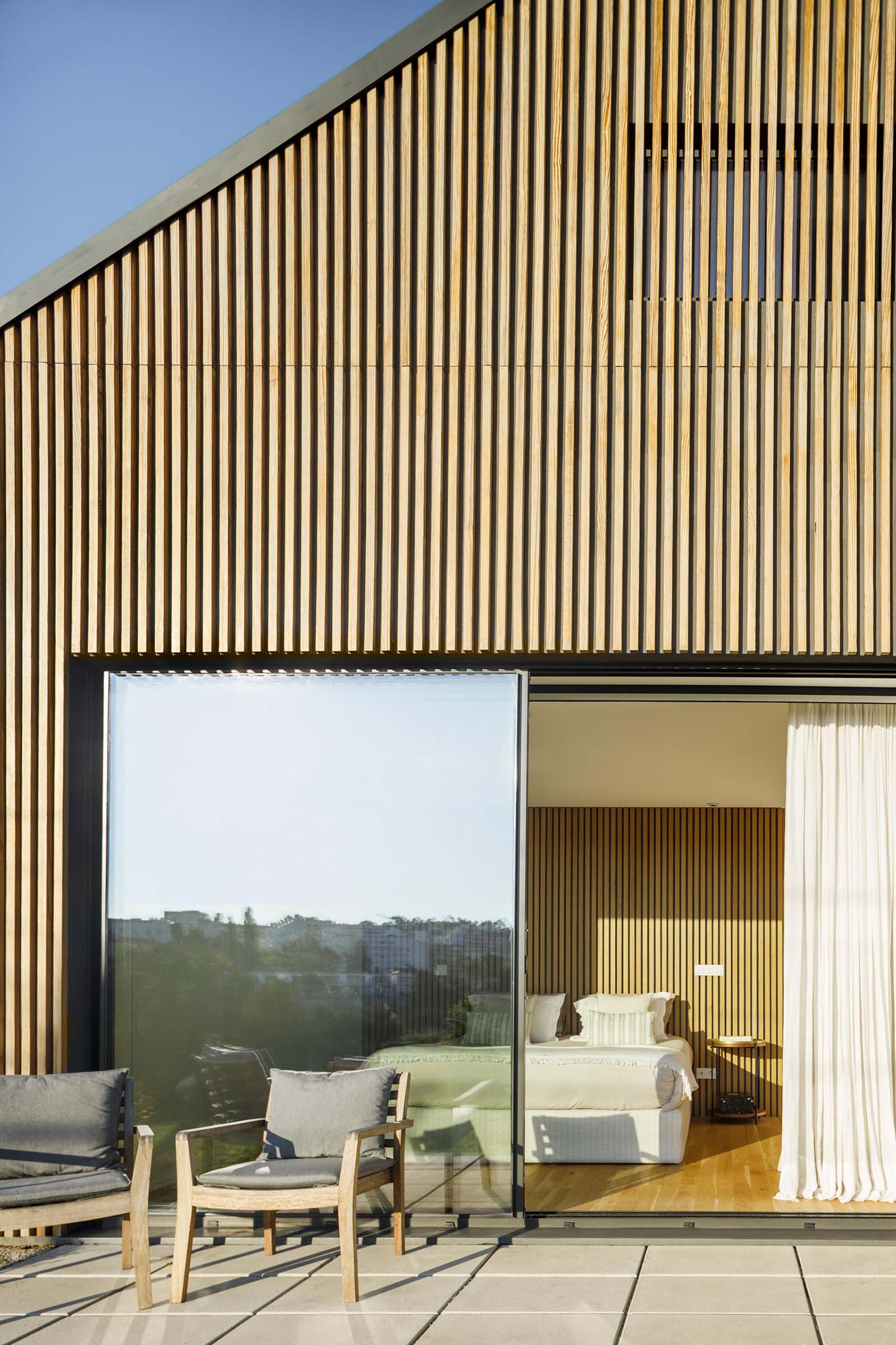 Современный дом с деревянным фасадом и большими раздвижными стеклянными дверями.