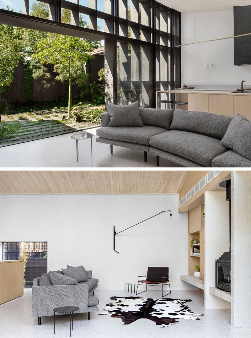 В этой современной гостиной, которая выходит на небольшой скульптурный задний двор, есть серый изогнутый диван, который расположен с видом на черный камин.