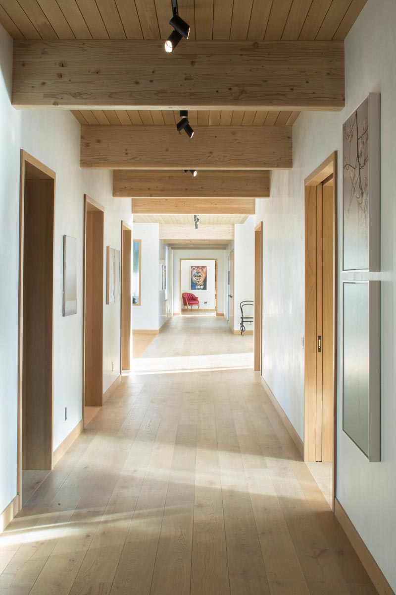 Коридор, проходящий по всей длине этого дома, имеет двери с деревянными рамами, которые обеспечивают доступ к различным другим частям дома. #ModernHallway #WoodFloors
