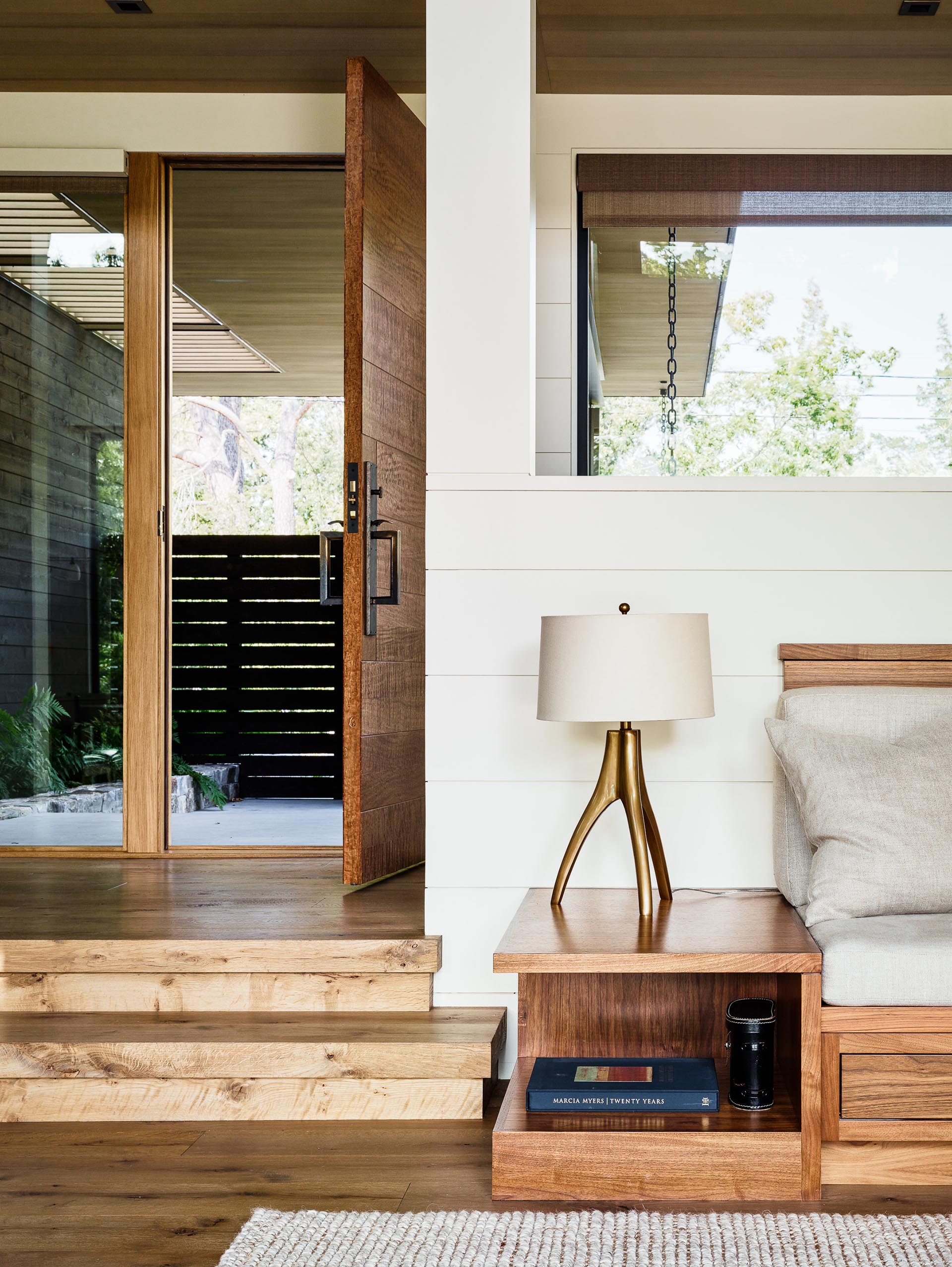 Светлый интерьер с деревянной входной дверью, деревянным полом и деревянным каркасом дивана.