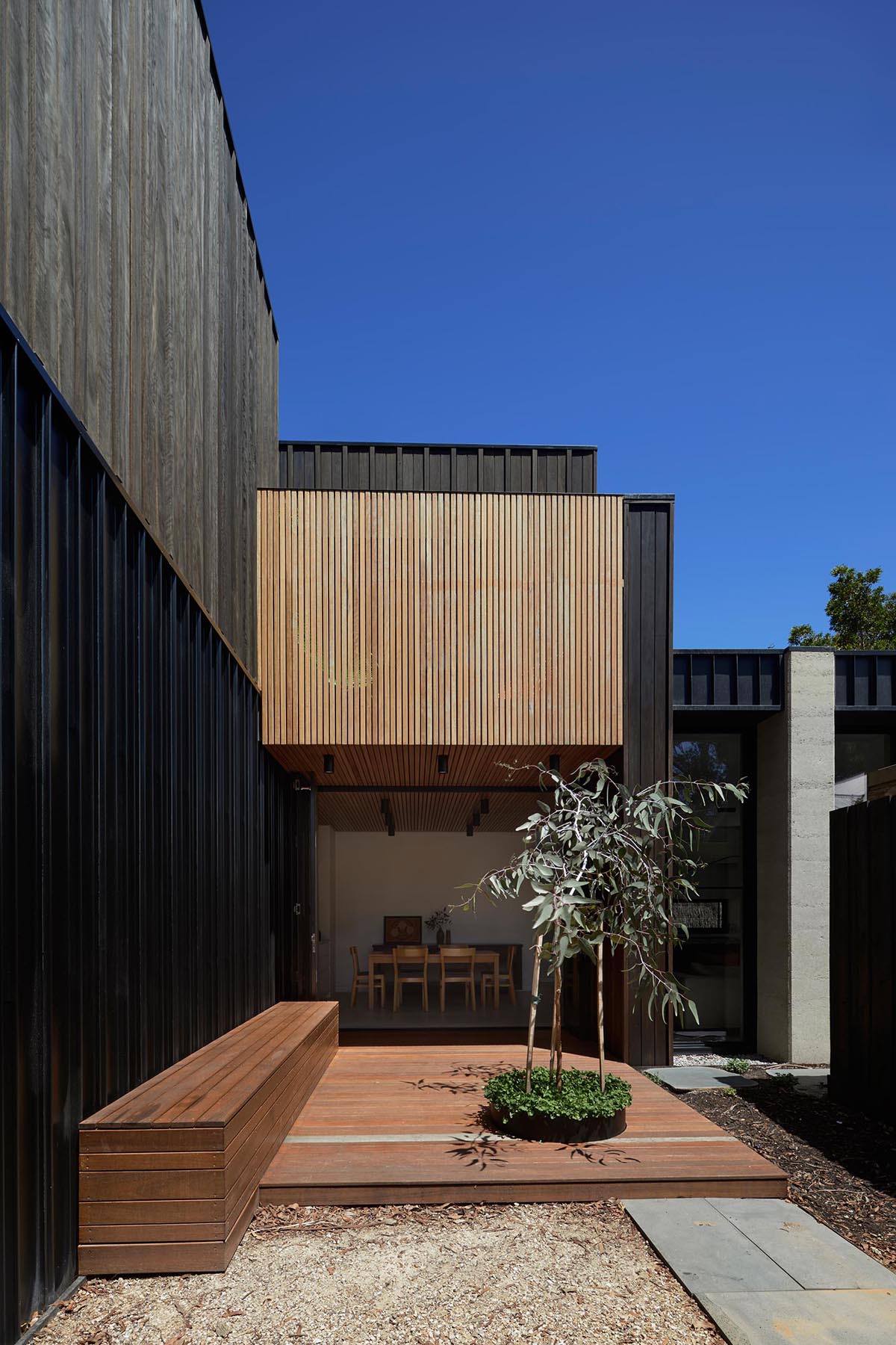 Современный дом с фасадом из темного дерева и бетона и террасой со встроенной скамейкой из осветительного дерева.
