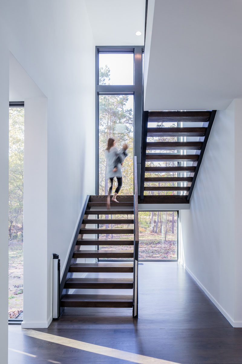 Лестница из темного дерева сильно контрастирует с белыми стенами в этом современном доме и ведет на верхний этаж дома. Окна выходят на высоту лестницы и пропускают много естественного света.