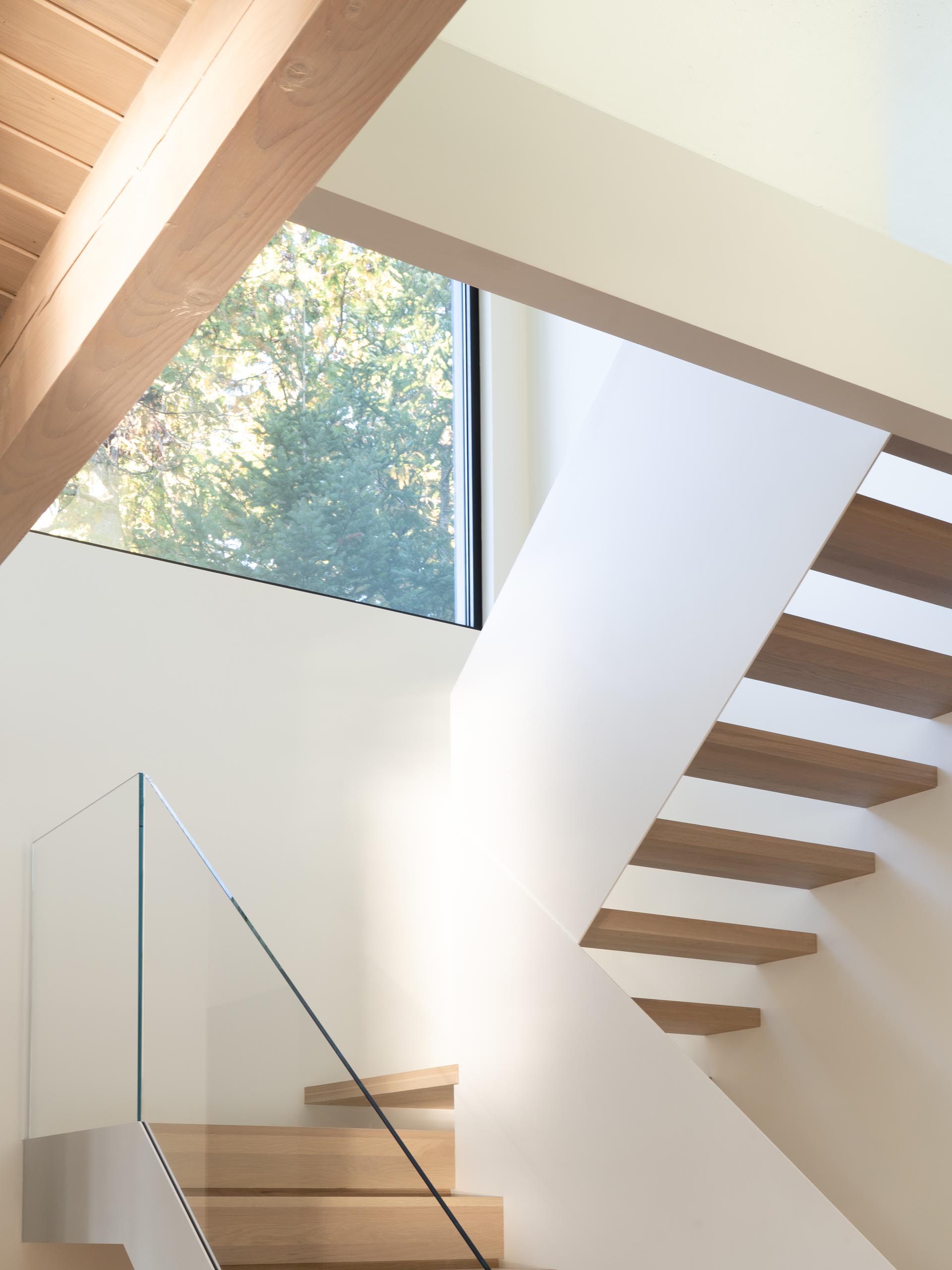 Современные белые лестницы с деревянными ступенями и стеклянными перилами.