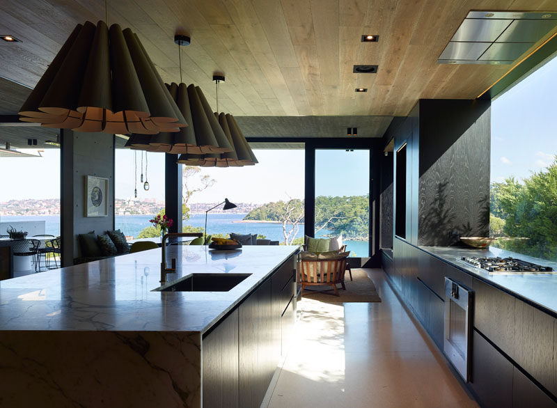 На этой современной кухне мебель из темного дерева контрастирует со светлым полом и потолком, а большое панорамное окно обеспечивает хорошее естественное освещение. #KitchenDesign #ModernKitchen