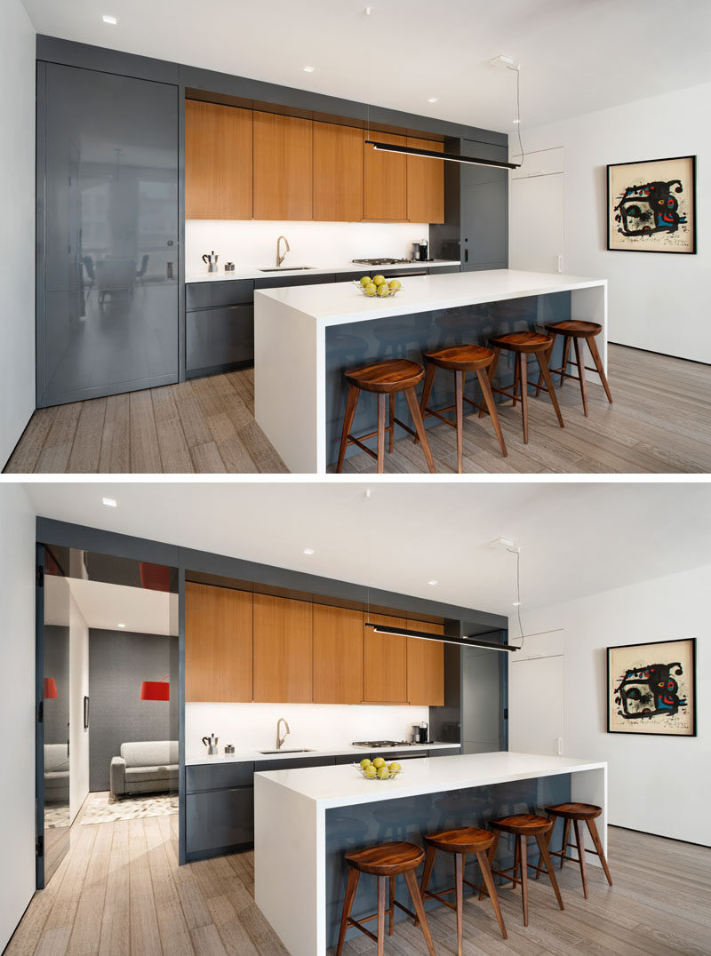Идеи для кухни. В этой современной кухне шкафы с глянцевым серым лаком дополняют телевизор в гостиной. Кухня также оснащена поворотными дверцами заподлицо с обеих сторон, которые выглядят как часть кухонного шкафа. Одна из дверей ведет в скрытый кабинет, а другая ведет в гостевую ванную комнату. #KitchenIdeas # ModernKitchen # GreyCabinets #KitchenIsland