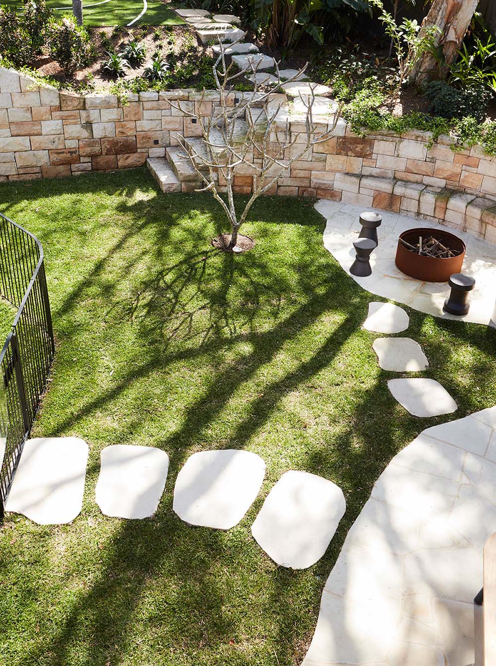 Стена из песчаника включает места для сидения вокруг костровой ямы и включает ступеньки, ведущие на верхний уровень сада.