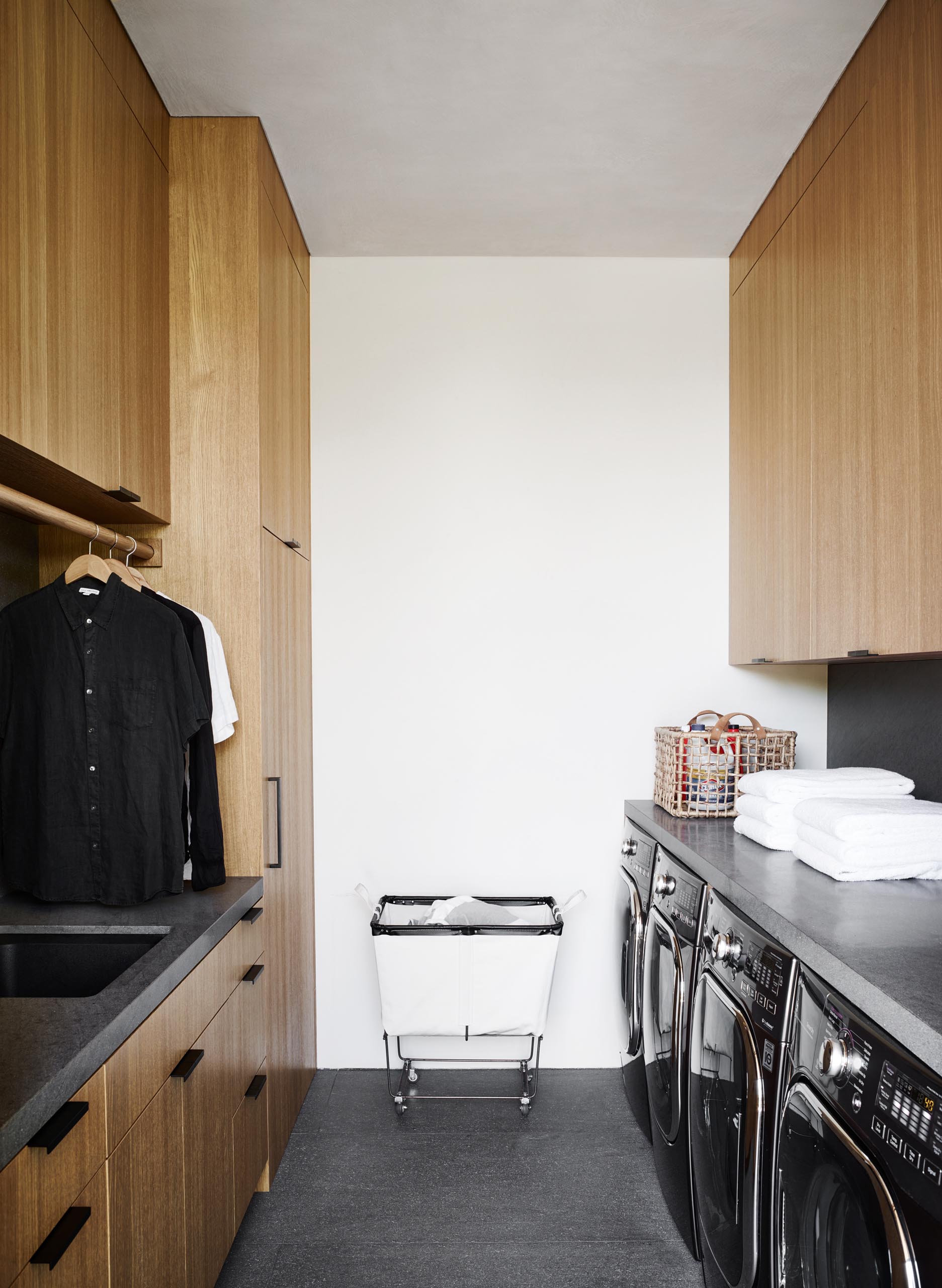 Современная прачечная с деревянными шкафами от пола до потолка, серыми столешницами и соответствующей серой плиткой на полу.