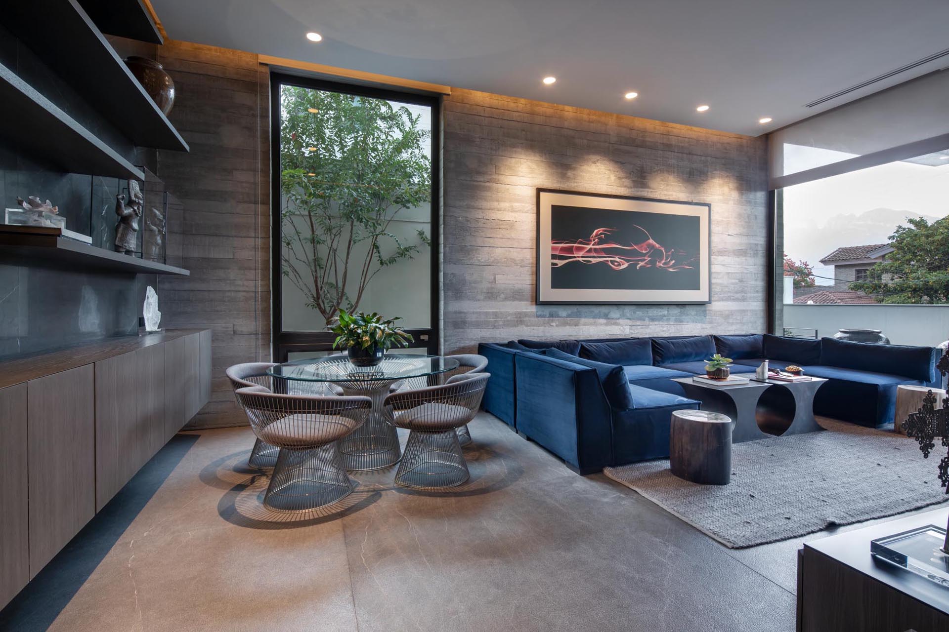 Современная гостиная с U-образным синим диваном, обеденной зоной и бетонной стеной в форме доски.