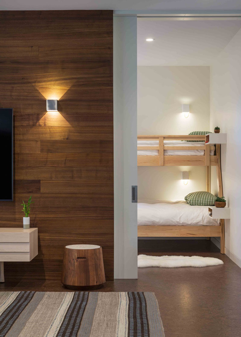 В этом современном доме есть гостевая комната с двухъярусными кроватями, которая расположена рядом с простой гостиной. #BunkBeds #PocketDoor #WoodAccentWall
