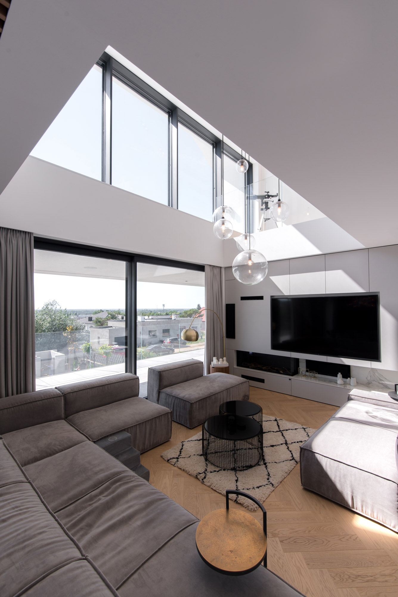 Гостиная, обставленная большим модульным диваном, создает много места для отдыха. Пустота в потолке двойной высоты позволяет проникать естественному свету из верхних окон.