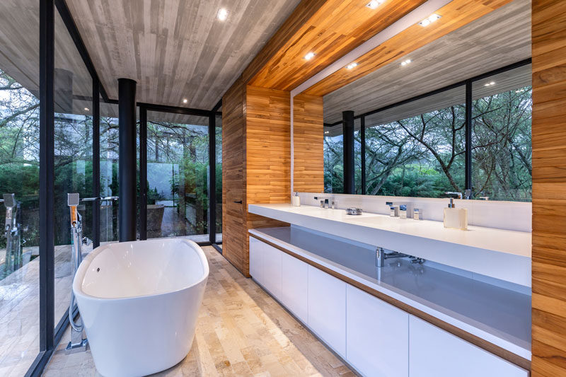В этой современной главной ванной комнате есть отдельно стоящая ванна и длинный туалетный столик с большим зеркалом, отражающим верхушки деревьев. # МастерВанная # ВаннаяДизайн # СовременнаяВанная