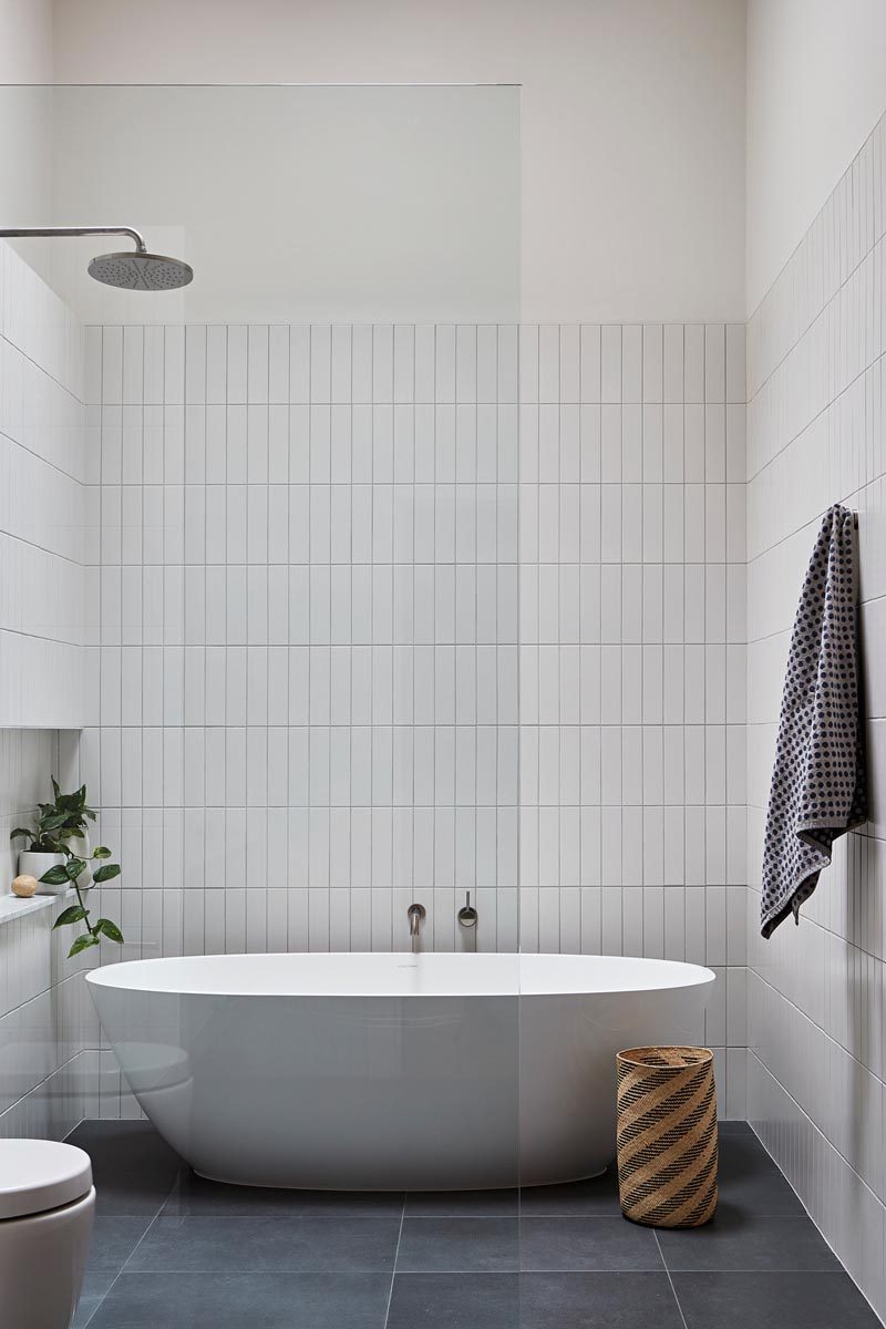 В этой современной главной ванной комнате вертикально уложена простая прямоугольная белая плитка, а пол покрыт каменной плиткой Signorino. Отдельно стоящая ванна делит пространство с душем, а встроенная ниша образует полку для растений и предметов ванной. # Современная ванная # Дизайн ванной