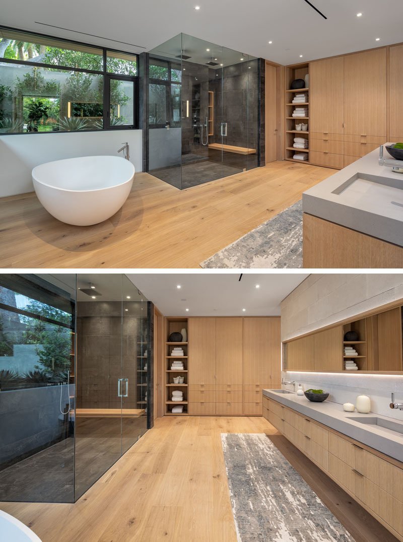 Современная ванная комната со скульптурной отдельно стоящей белой ванной, застекленной душевой кабиной для двоих, окнами с видом на растения снаружи и деревянной мебелью.