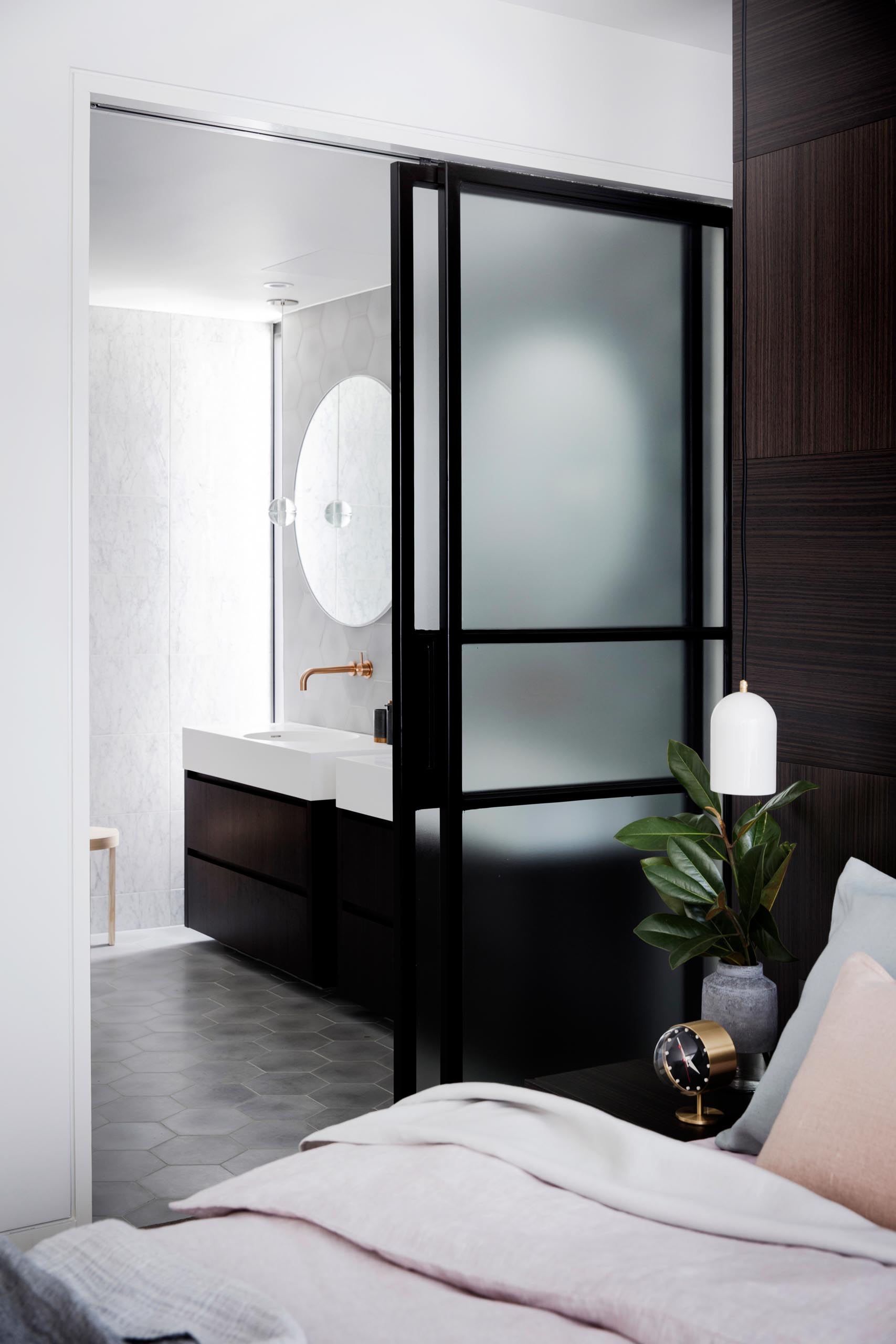 Дверь из матового стекла в черной рамке, которая открывается, открывая современную ванную комнату.