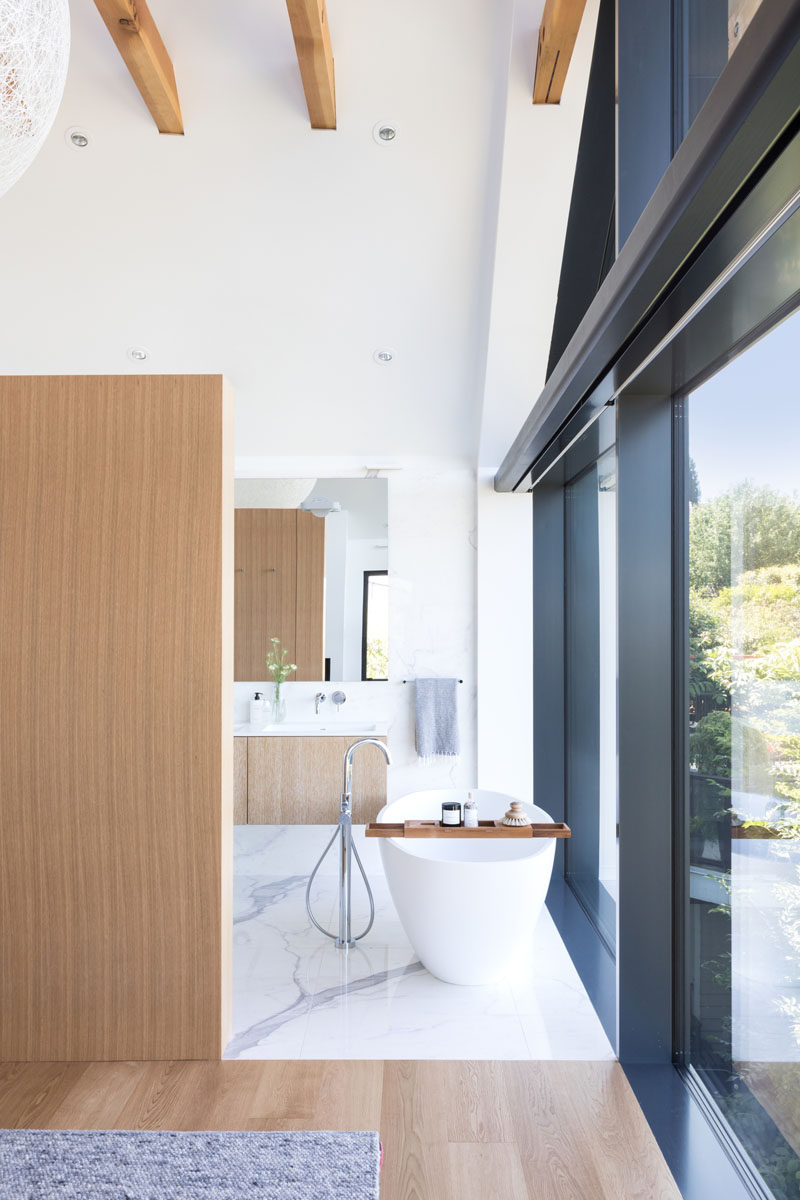 В этой современной ванной комнате перед окнами установлена ​​отдельно стоящая белая ванна, чтобы можно было любоваться красивым видом, а за стеной - туалетный столик, туалет и душевая кабина. # Ванная # Современная # Ванна # Отдельностоящая