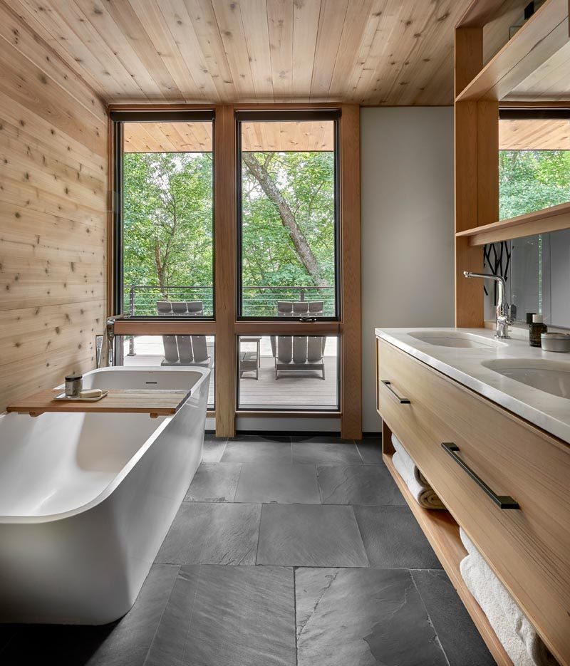 В этой современной главной ванной комнате отдельно стоящая ванна оборудована окнами, выходящими на небольшую террасу. Напротив ванны стоит деревянный туалетный столик с двойной раковиной, ящиками для хранения вещей и открытыми стеллажами. # МастерВанная # ВаннаяДизайн