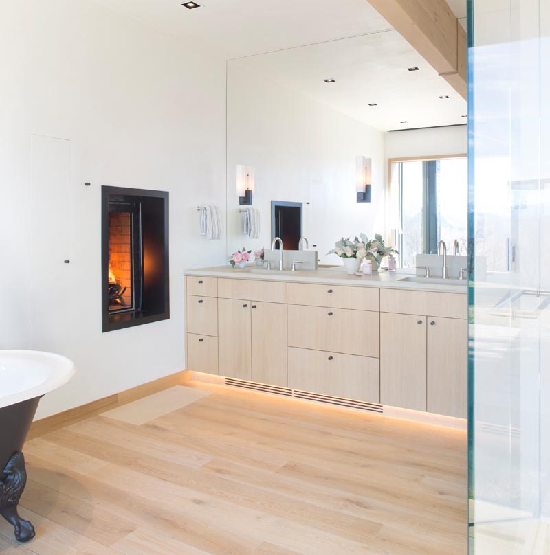 В этой современной главной ванной комнате деревянный туалетный столик находится под зеркалом во всю стену, которое отражает свет из окна, а камин добавляет в пространство тепла и ощущения расслабления. # МастерВанная # Дизайн ванной # ДеревоТаня # Камин