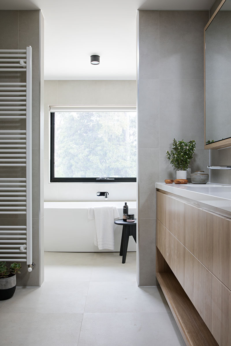 В этой современной ванной комнате туалетный столик из светлого дерева и растения добавляют естественности серо-белой ванной комнате.
