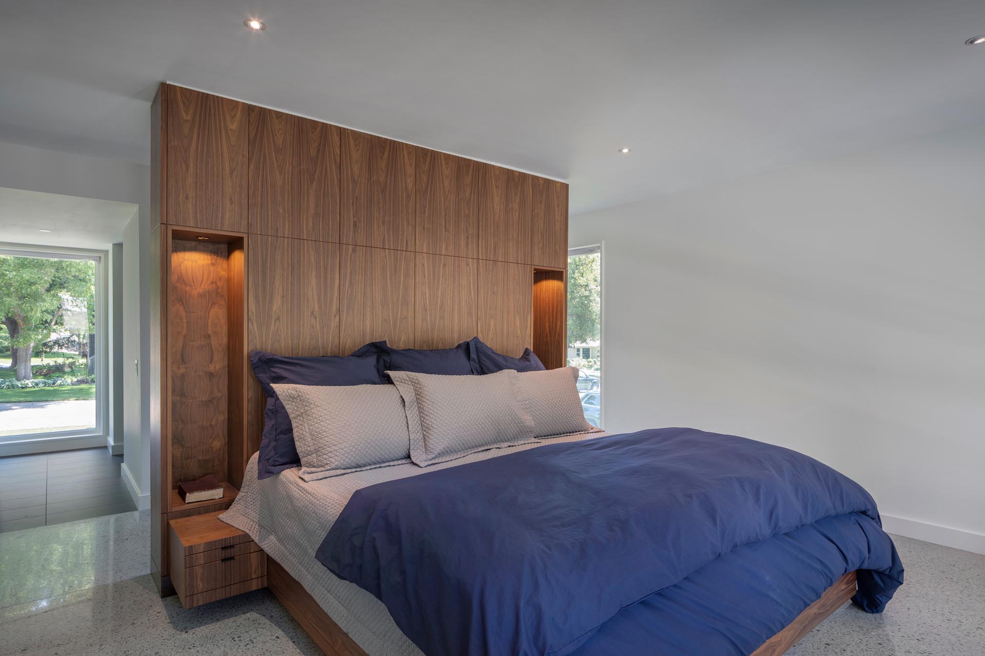 Современная спальня с деревянной акцентной стеной с пустотами, позволяющими установить прикроватные лампы.
