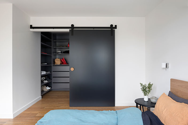 В этой современной главной спальне есть большая гардеробная, спрятанная за матовой черной раздвижной дверью сарая.