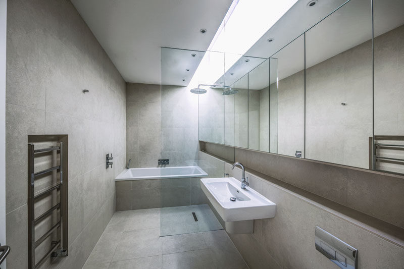  В этой современной ванной комнате установлен световой люк, создающий яркую полосу естественного света, которая скрашивает нейтральную цветовую палитру. Стена из зеркал проходит по всей длине комнаты, а стеклянная перегородка отделяет влажные зоны от остальной части ванной комнаты 