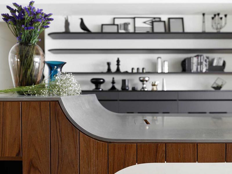 Этот современный многоэтажный кухонный остров с основанием, облицованным вертикальным темным деревом и бетонной столешницей, имеет небольшую барную раковину и зону для приготовления еды на одном конце и консольный обеденный стол на другом. #MultiHeightKitchenIsland #KitchenIslandDesign # CantileveredDiningTable #KitchenDesign # ModernKitchen #KitchenIslandIdeas