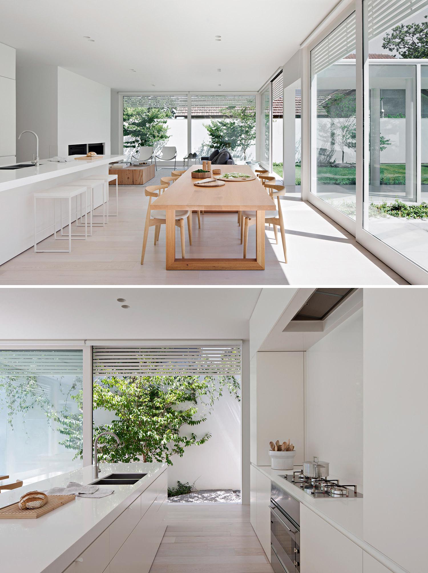 Современный интерьер открытой планировки с большим деревянным обеденным столом и минималистской белой кухней.