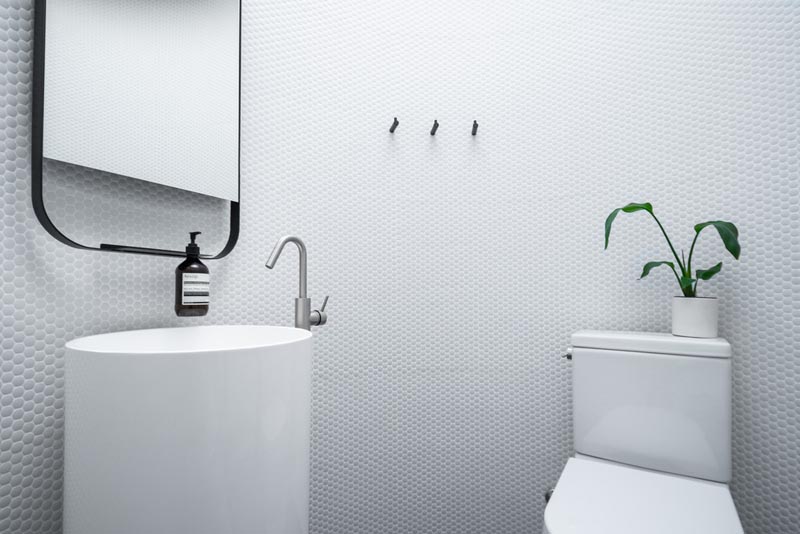 Эта современная круглая ванная комната имеет стены, выложенные белой плиткой, изогнутую тумбу с зеркалом с закругленными краями и туалет. # Ванная # КруглаяВанная # Плитка Пенни # Пьедестал