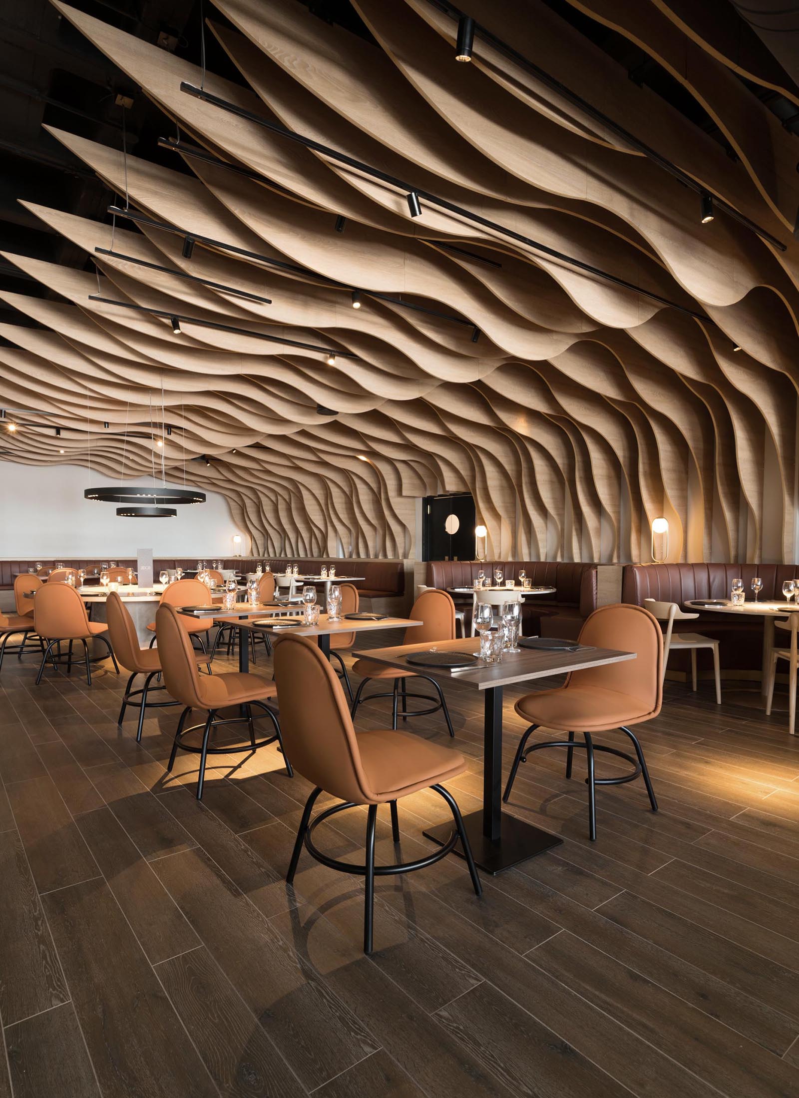 Современный ресторан со скульптурными деревянными ребрами, которые покрывают стены и потолок и гармонируют с окружающей мебелью.
