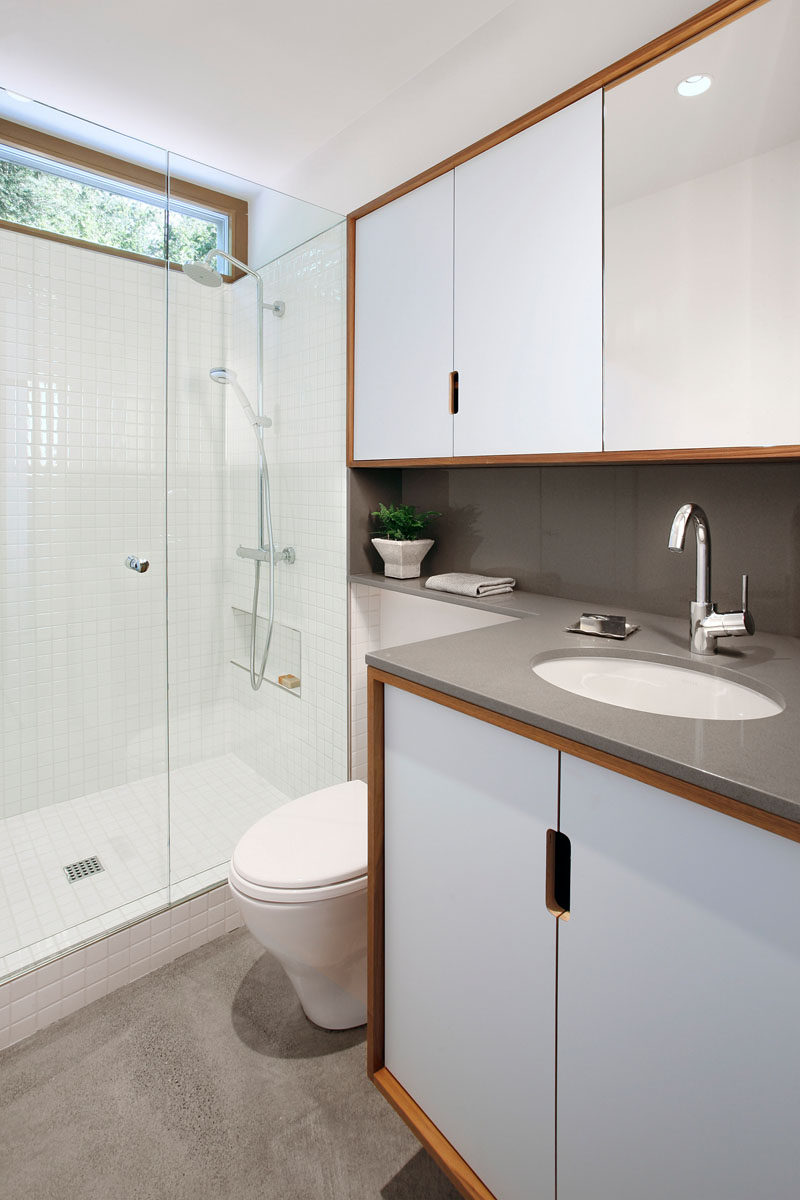  В этой современной ванной комнате серая столешница сочетается с белой плиткой, стеклом и деревянными рамами, чтобы создать современный вид. # Современная ванная # Дизайн ванной 