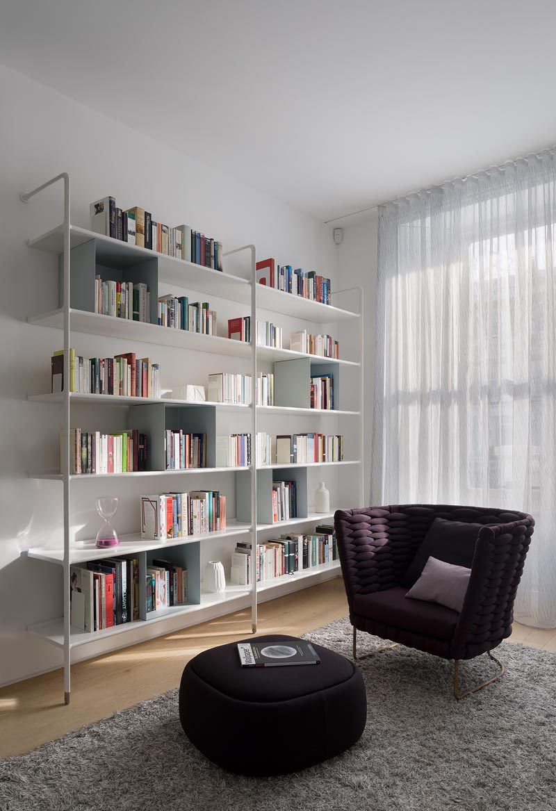 В этой современной гостиной есть белые открытые книжные полки и удобное кресло с соответствующей подставкой для ног. # Гостиная # Библиотека # Стеллажи