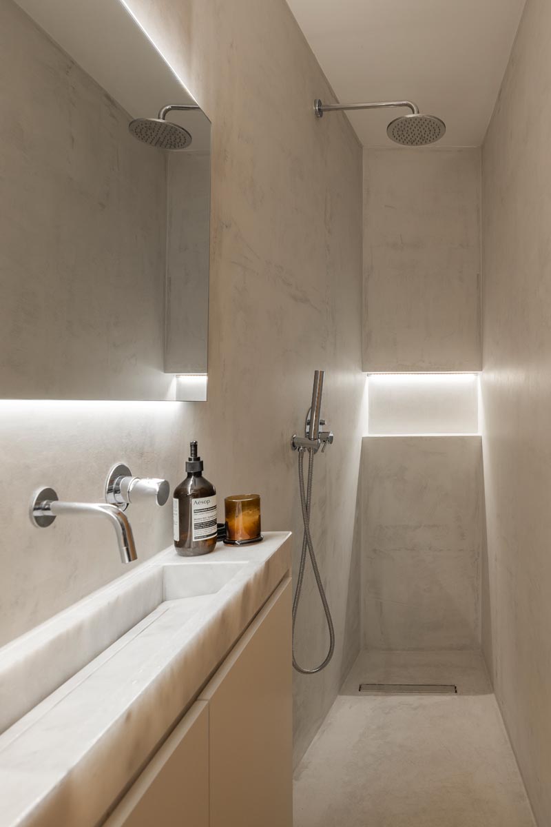 Эта небольшая и узкая современная ванная комната имеет длинный тонкий туалетный столик вдоль одной стены, с душем на одном конце и туалетом на другом. Скрытая подсветка за зеркалом и в душевой нише помогает сохранить светлое пространство. # МаленькаяВанная # УзкаяВанная # Дизайн ванной # СкрытоеОсвещение # НевидимыйСлив