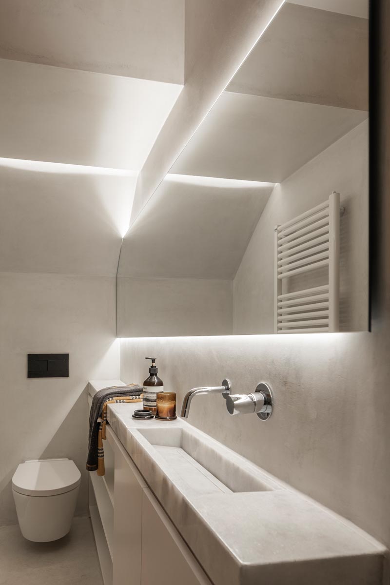 Эта небольшая и узкая современная ванная комната имеет длинный тонкий туалетный столик вдоль одной стены, с душем на одном конце и туалетом на другом. Скрытая подсветка за зеркалом и в душевой нише помогает сохранить светлое пространство. # МаленькаяВанная # УзкаяВанная # Дизайн ванной # СкрытыйВаннаяОсвещение