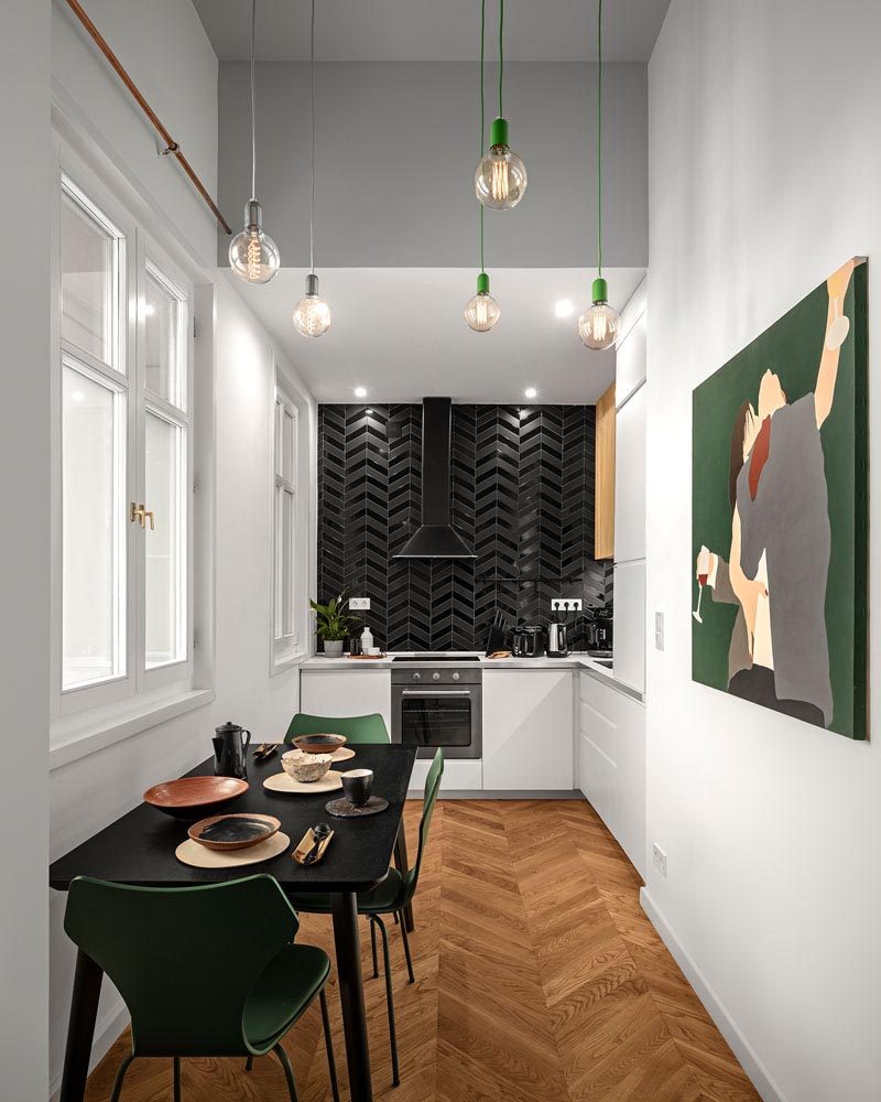 Глянцевая и матовая черная плитка были использованы для создания акцентной стены на этой современной кухне с минималистскими белыми шкафами и черным обеденным столом. # Кухня #BlackTiles #WhiteCabinets