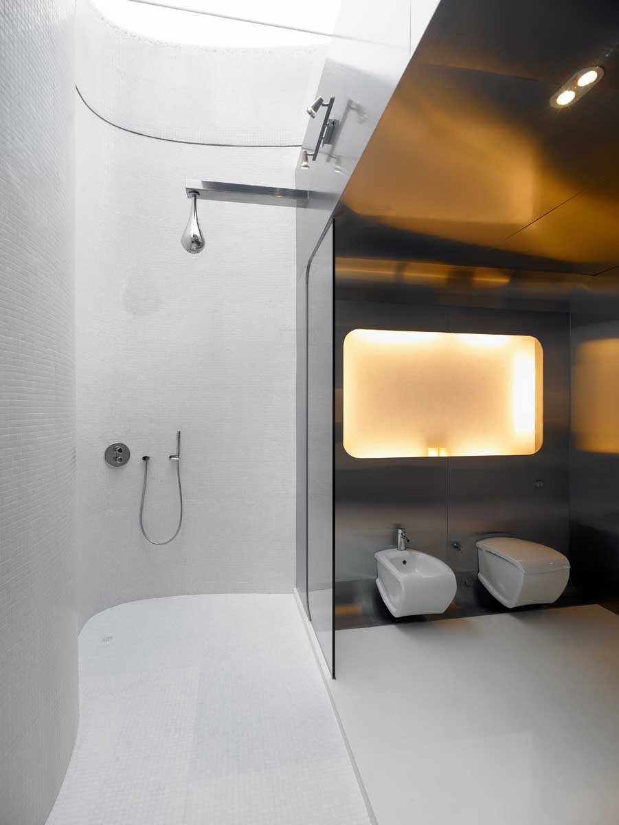 Современная ванная комната со стенами из нержавеющей стали, изогнутыми плиточными стенами, стеклянными перегородками для душа и двойным душем с потолочным окном.