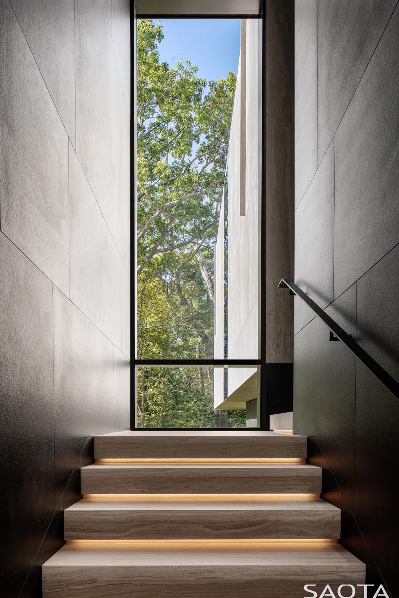 Эта современная лестница облицована теми же керамическими панелями, что и фасад дома, в то время как деревянные ступени лестницы имеют скрытое освещение под ними, а из высокого окна открывается вид на деревья. #StairDesign #TallWindow #StairWithLighting