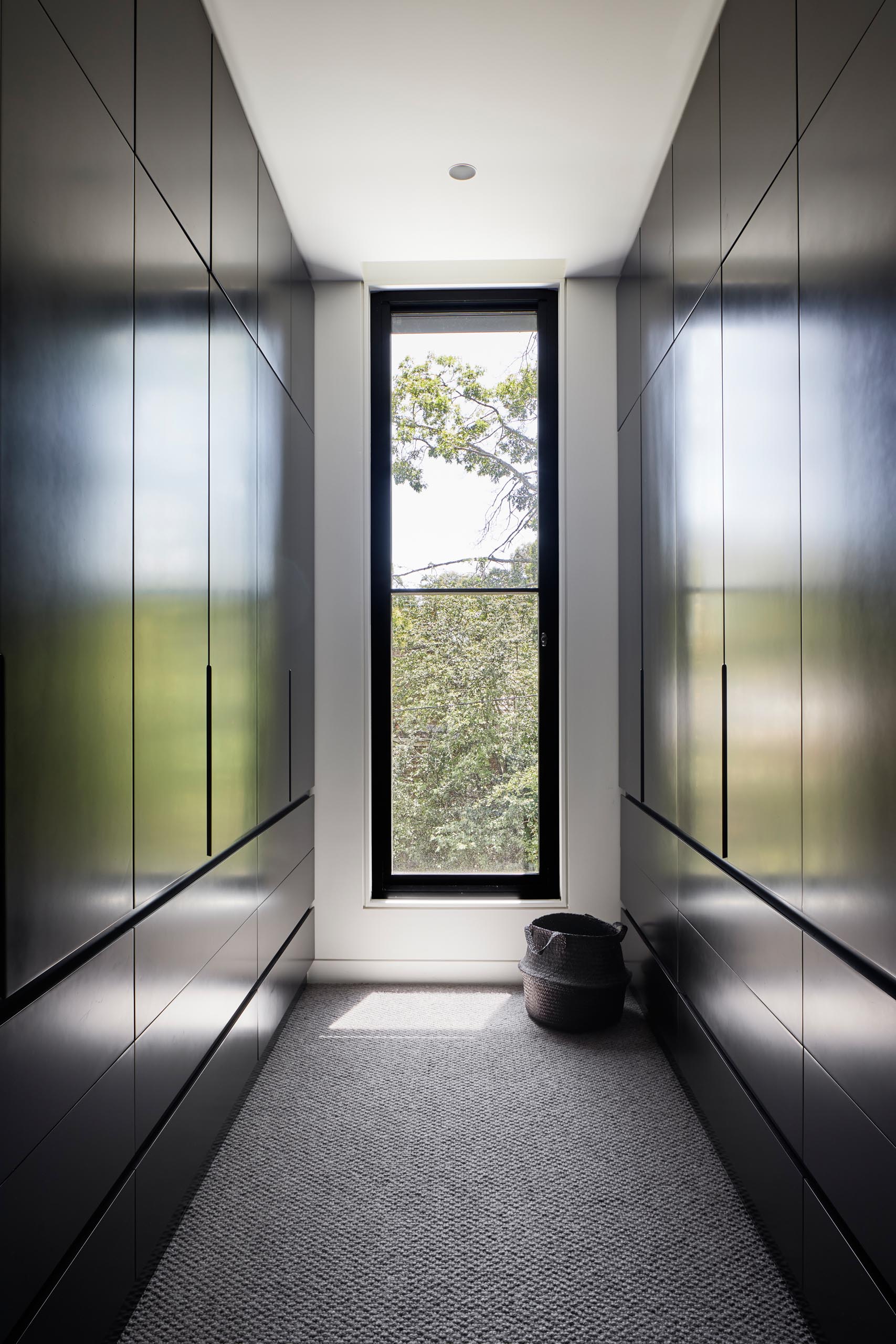 В этой современной гардеробной есть темные шкафы от пола до потолка, которые выравнивают стены и позволяют взгляду сосредоточиться на виде дерева через окно.