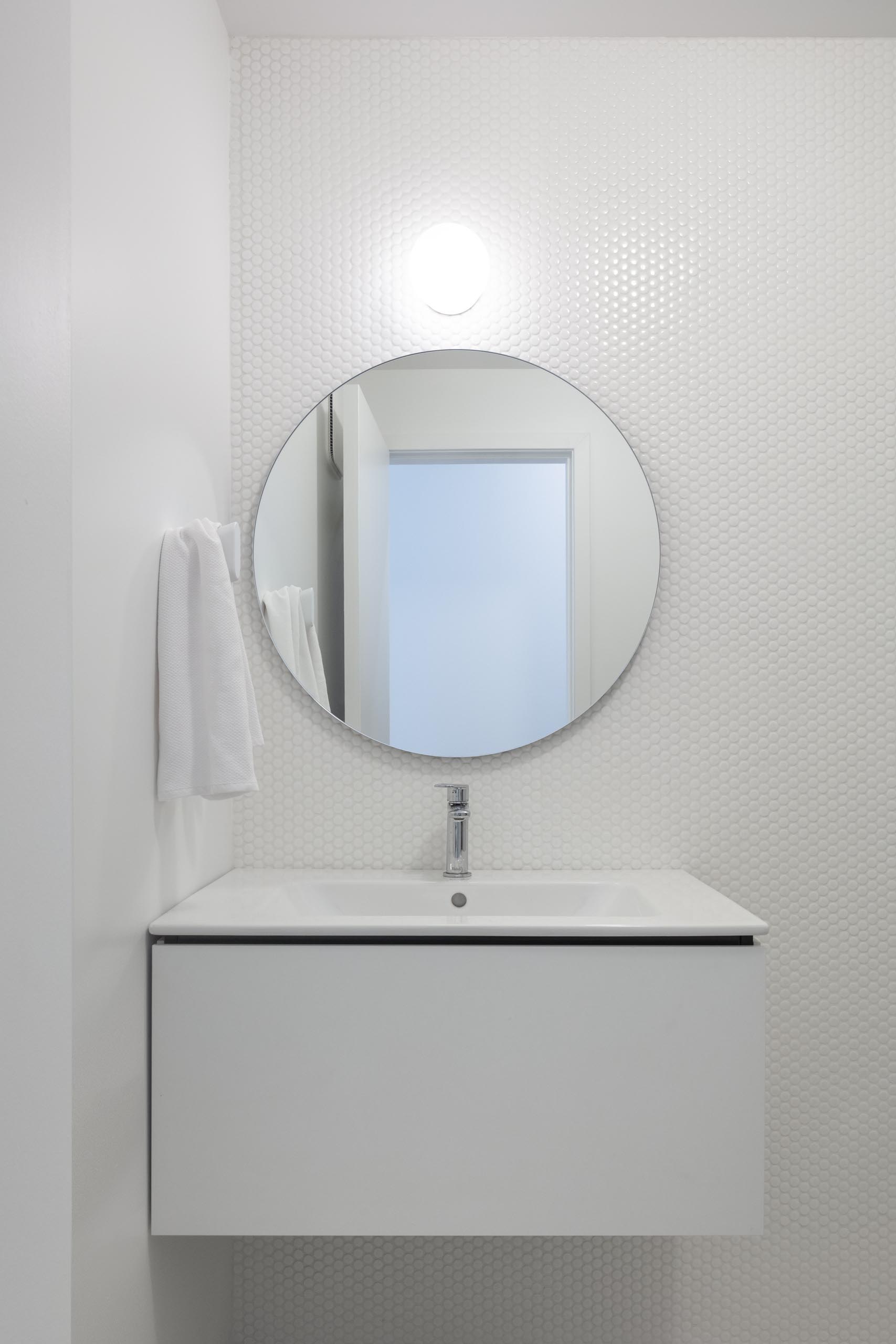 Современная белая ванная комната с белой плиткой и круглым зеркалом.