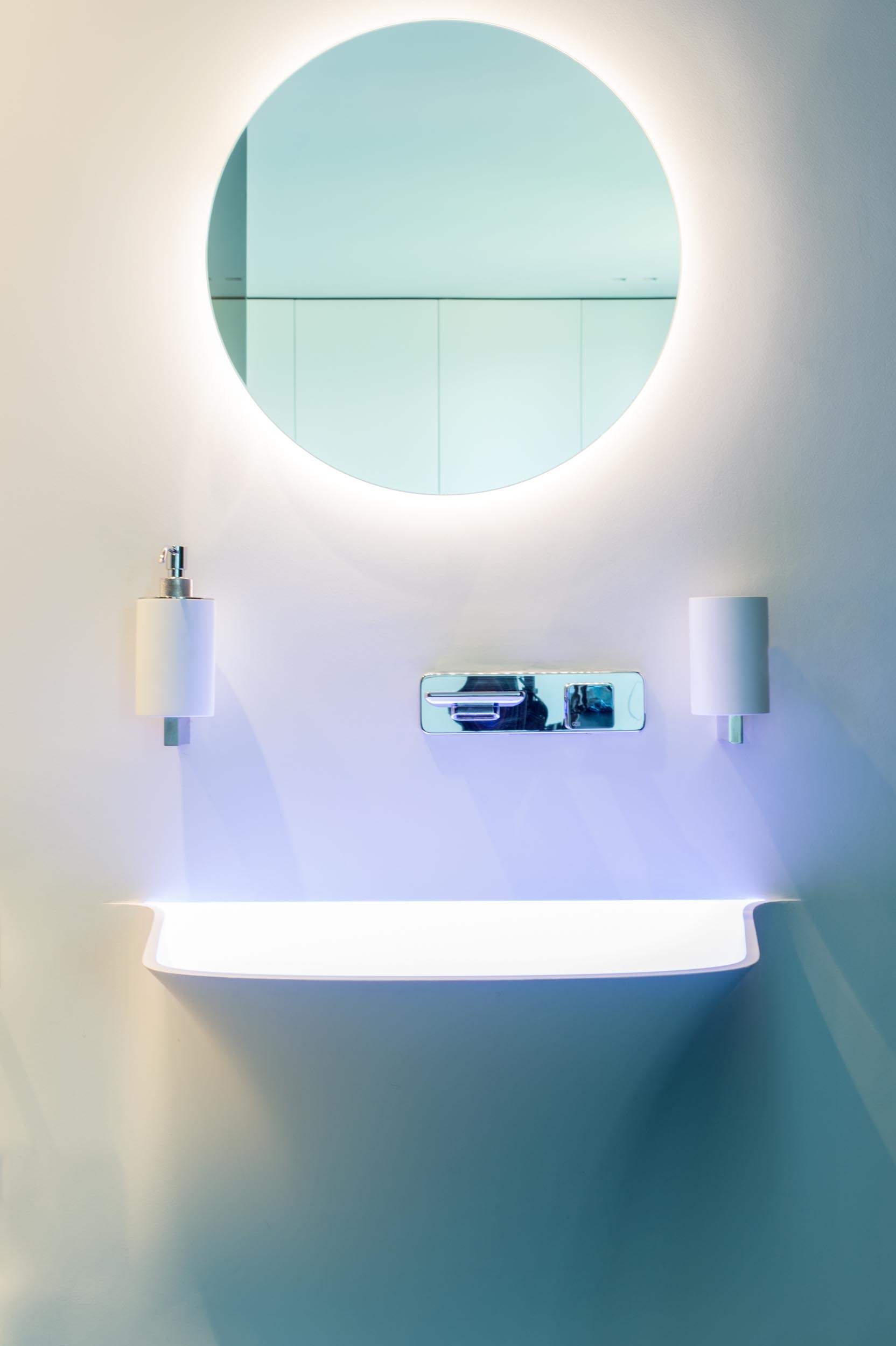 Современная ванная комната с бесшовным белым туалетным столиком и круглым зеркалом с подсветкой.