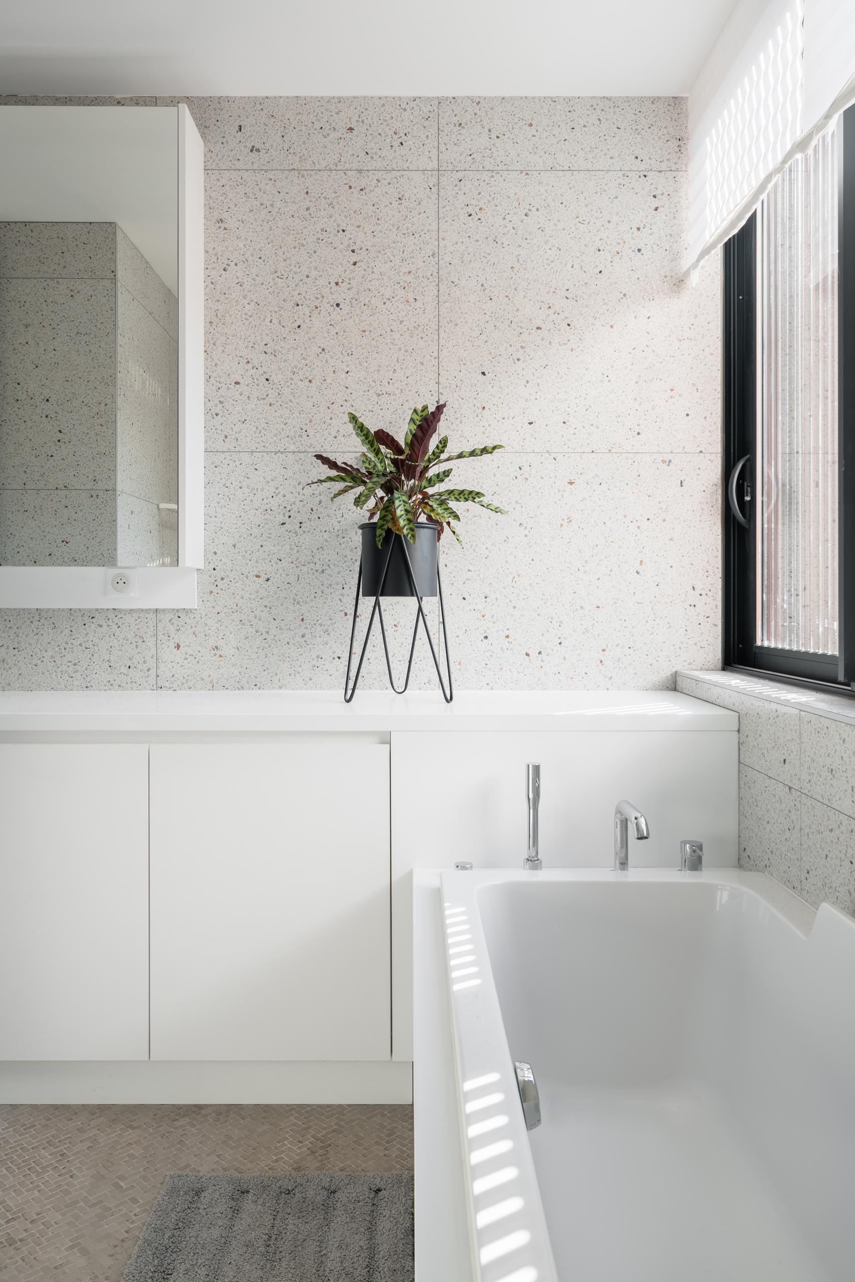 Современная ванная комната со светлыми стенами, белой мебелью, большим зеркалом и встроенной ванной.