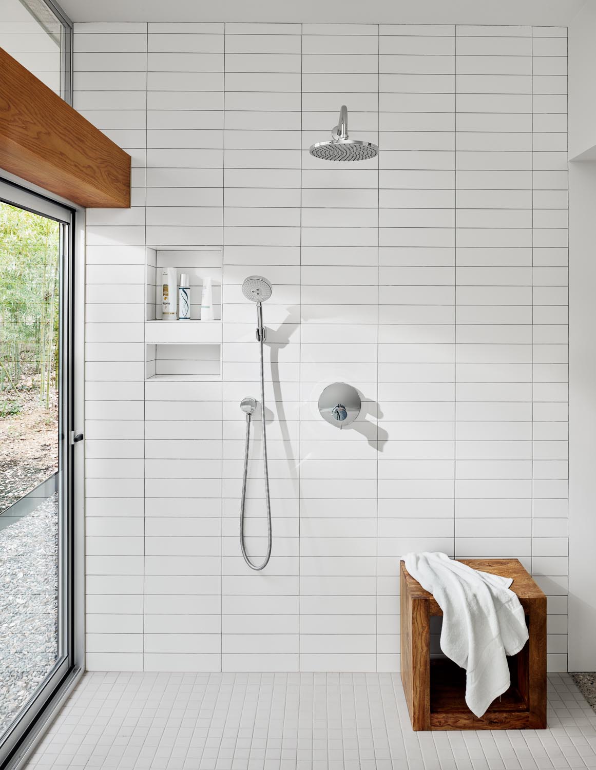 В этой современной ванной комнате есть парящий деревянный туалетный столик, встроенная ванна и стены, выложенные белой прямоугольной плиткой.