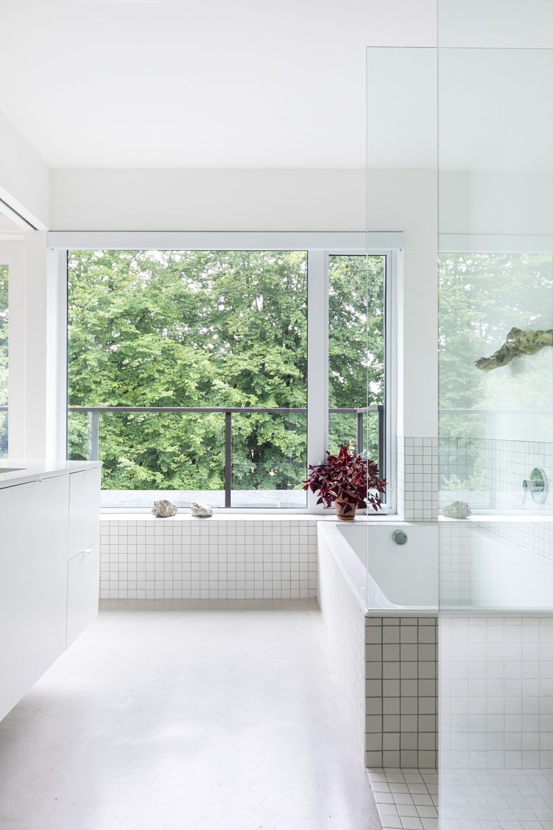 В этой современной ванной комнате большие окна выходят на деревья, а встроенная ванна, окруженная белой квадратной плиткой, примыкает к застекленной душевой кабине. #ModenВанная # БелаяВанная # Встраиваемая # Бетонные полы