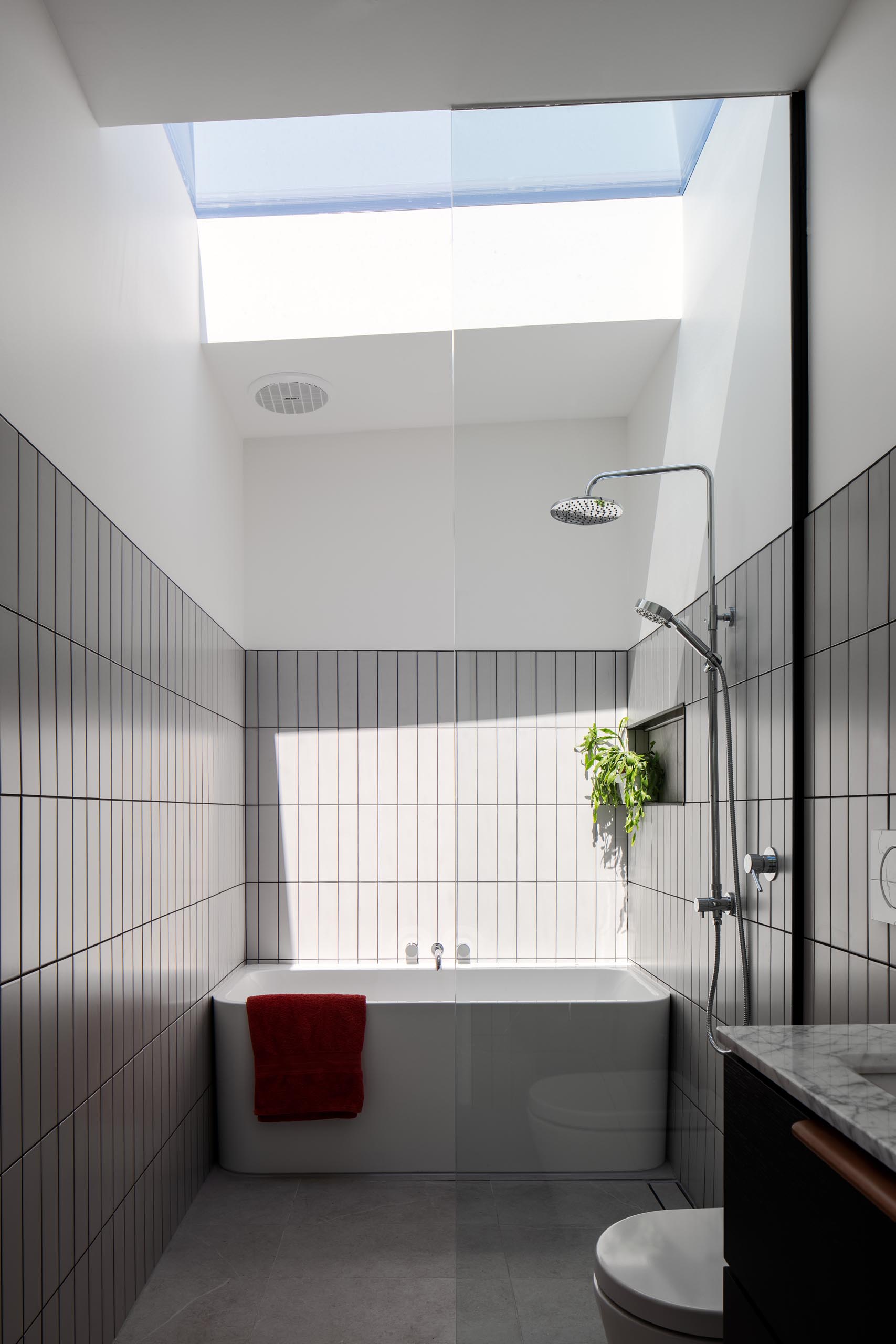 Современная ванная комната с серой плиткой, белой ванной и потолочным окном.