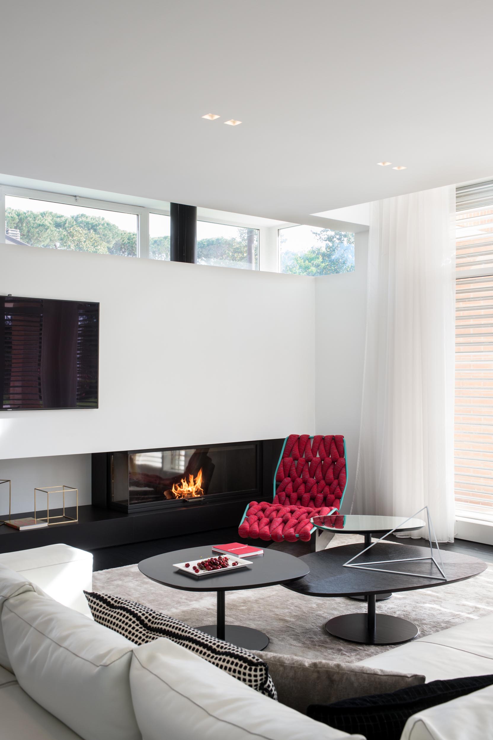 В этой современной гостиной белый угловой диван стоит на большом коврике, а черные журнальные столики дополняют черный камин. Чтобы добавить яркости, был выбран плетеный красный шезлонг.