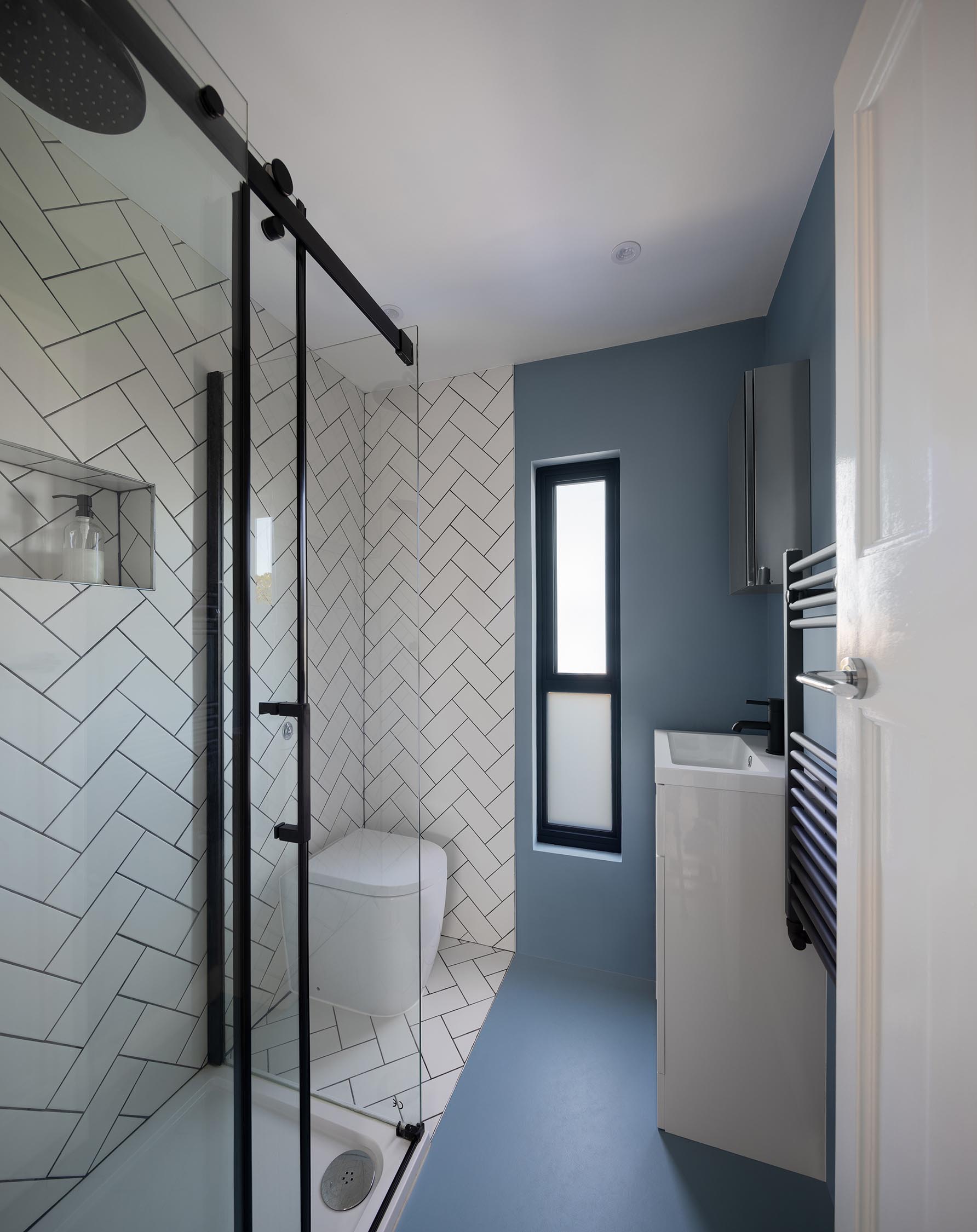 Современная ванная комната с белой плиткой в ​​елочку, черной фурнитурой и узким туалетным столиком.