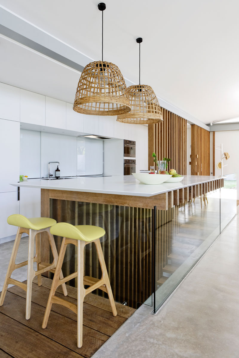 На этой современной кухне минималистичные белые шкафы украшают стену, а деревянные ребра и стекло столешницу кухонного острова. # СовременнаяКухня #KitchenDesign # БелаяКухня 